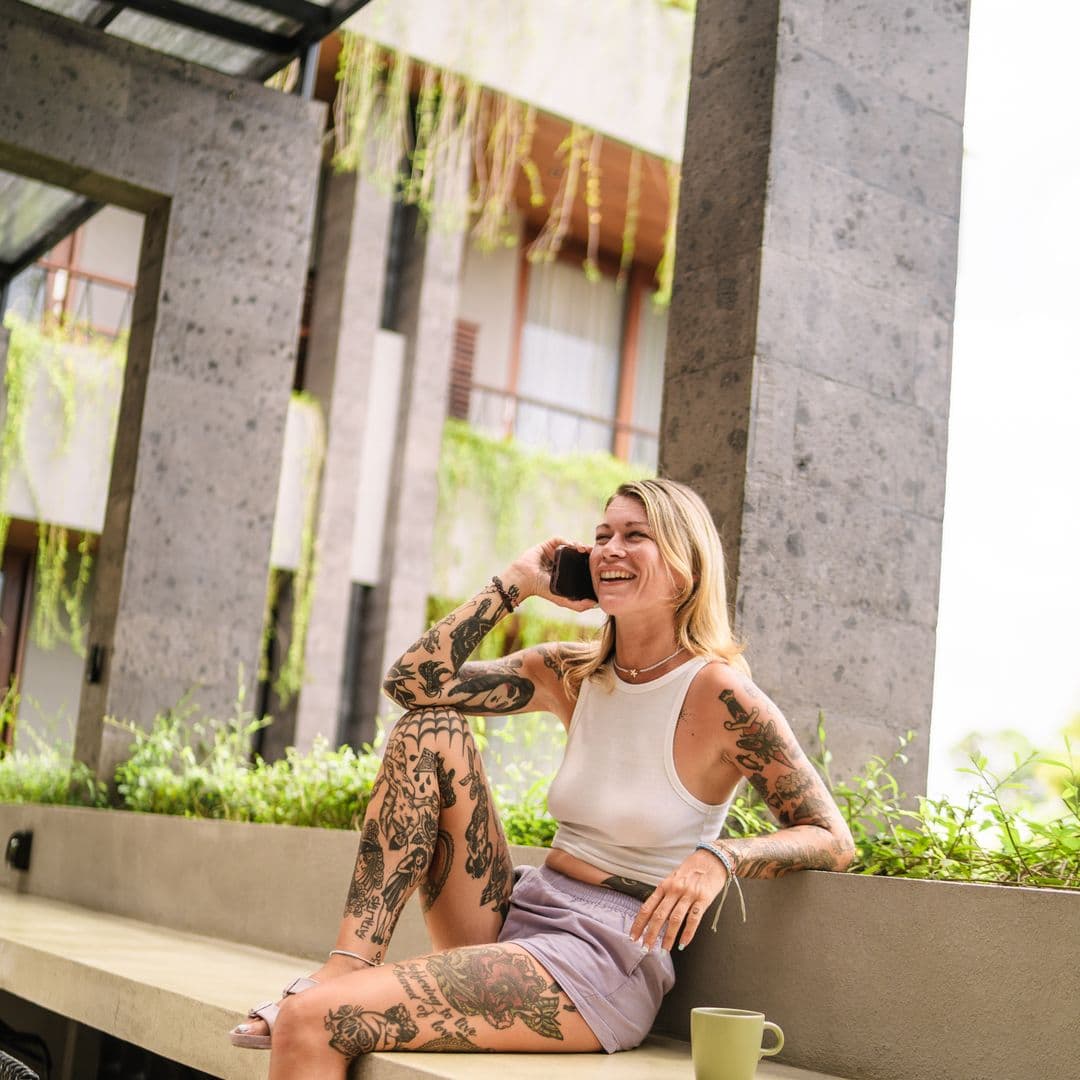 Guest laughing on a phone call during a coffee break on a planted ledge at TheHub