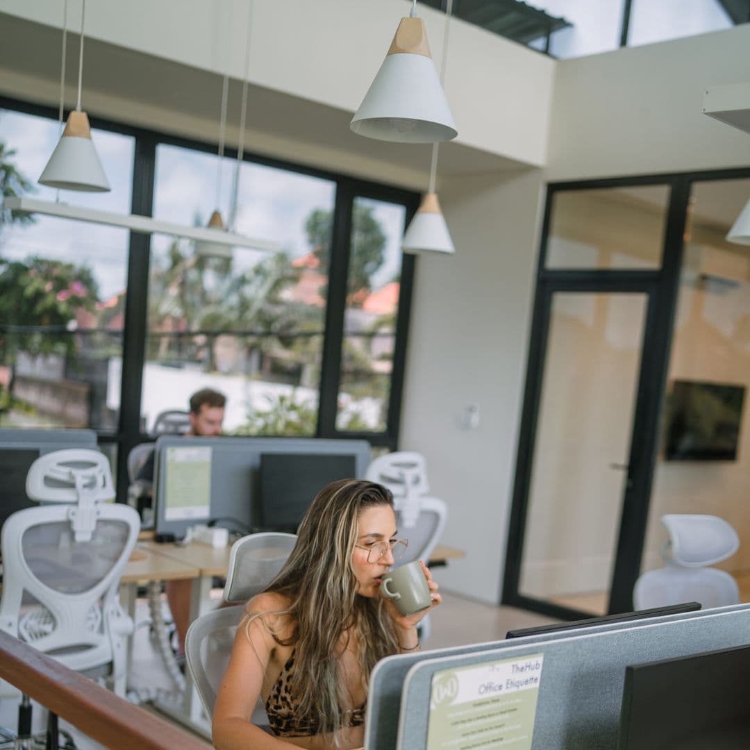 Guest working at a monitor in TheHub's coworking space with ergonomic chairs and garden views