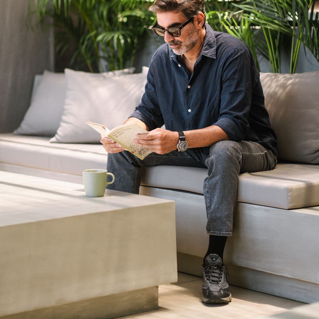 Guest reading a book with a coffee on TheHub's outdoor lounge sofa among palms
