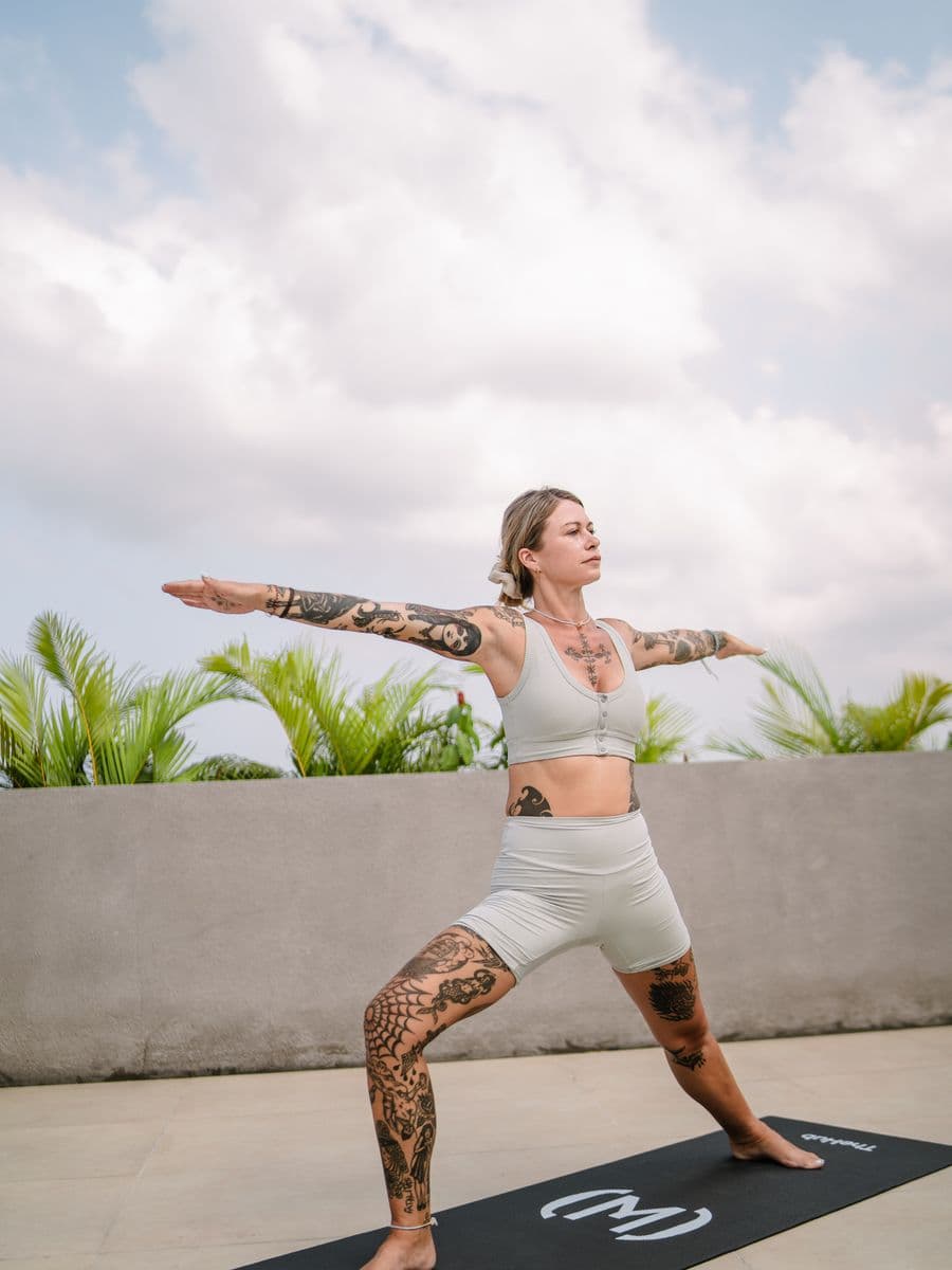 Guest holding a warrior pose on the rooftop deck in soft morning light