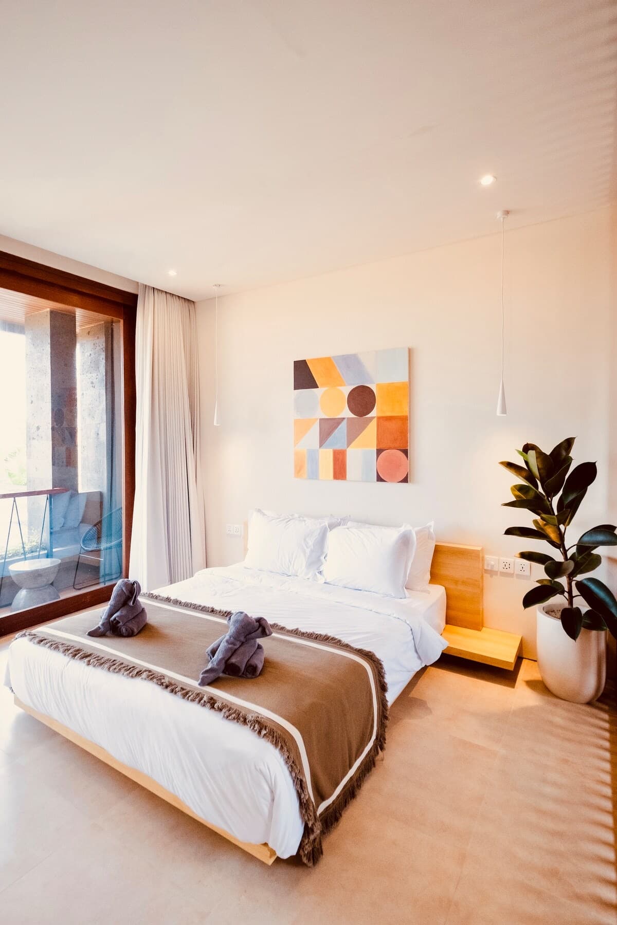 Queen bed with folded towel favours, a private balcony with rattan seating visible through the glass door