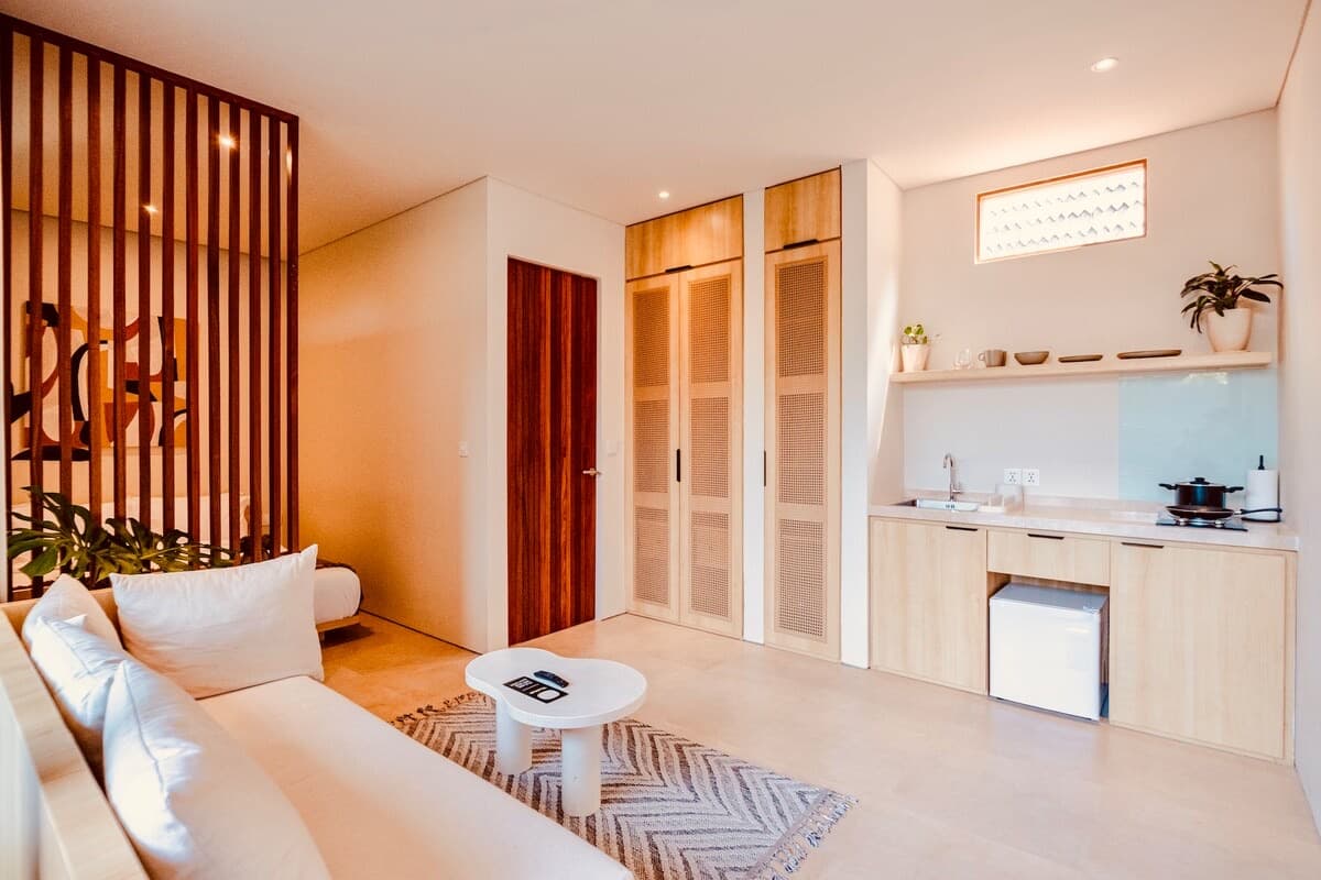 Timber-slat kitchenette with stovetop and shelving, opening onto the studio's linen sofa and coffee table