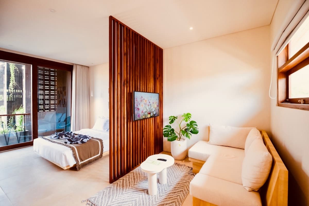 Studio bed and wood-slat partition opening onto a private balcony with blue rattan lounge chairs