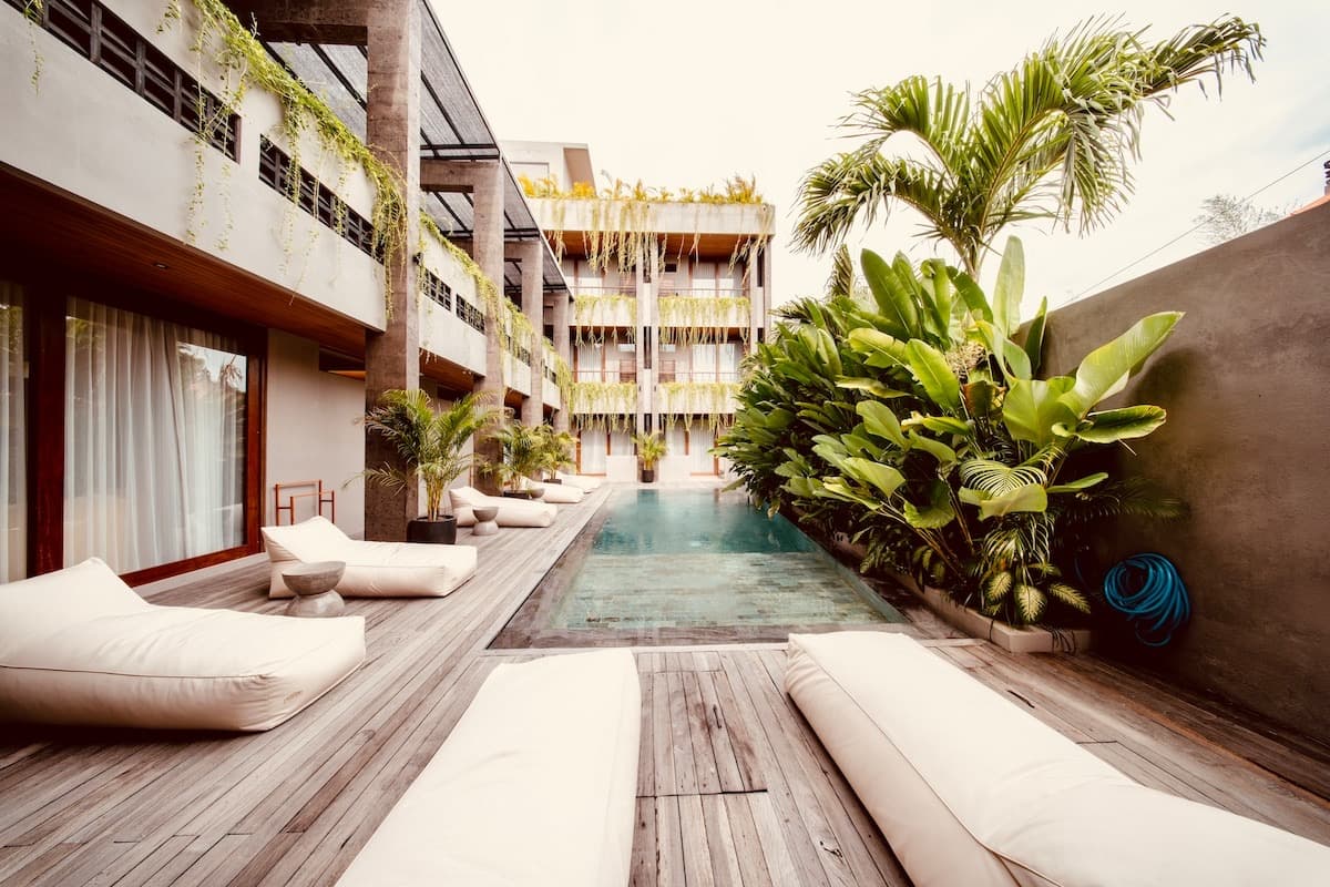 Ground-floor pool terrace lined with daybeds and palms, framed by the building's timber-screened facade